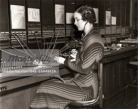 1930s WOMAN TELEPHONE OPERATOR SITTING AT LARGE MANUAL SWITCHBOARD DIRECTING CALLS