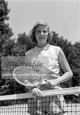 1950s PORTRAIT WOMAN HOLDING TENNIS RACQUET STANDING BEHIND NET OUTDOOR