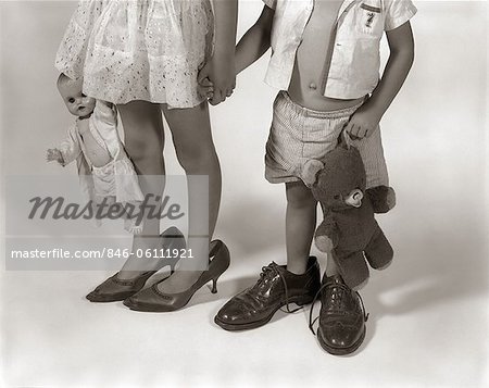 1950s 1960s CLOSE-UP OF LITTLE GIRL & BOY FROM NECK DOWN WEARING PARENTS' SHOES