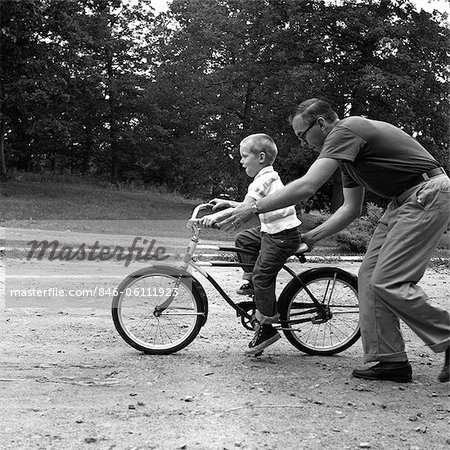 1960s FATHER GIVING SON ON BIKE A PUSH TEACHING HIM HOW TO RIDE BICYCLE