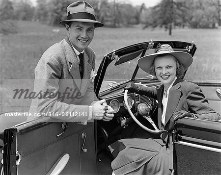 1930s 1940s PORTRAIT COUPLE MAN WOMAN TOGETHER WITH CONVERTIBLE AUTOMOBILE SMILING WEARING HATS LOOKING AT CAMERA