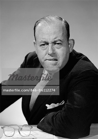 1950s 1960s PORTRAIT OF MAN BUSINESSMAN WORRIED UNHAPPY FROWNING LEANING ON DESK LOOKING AT CAMERA