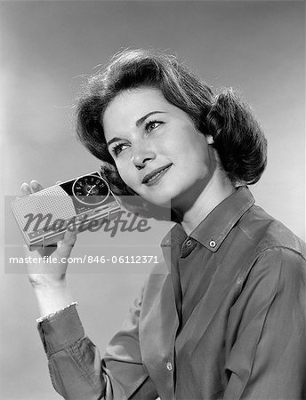 1960s PORTRAIT OF SMILING TEENAGE GIRL TILTING HEAD TO LISTEN TO PORTABLE RADIO HELD IN HAND TO EAR 1960s PORTRAIT OF SMILING TEENAGE GIRL TILTING HEAD TO LISTEN TO PORTABLE RADIO HELD IN HAND TO EAR