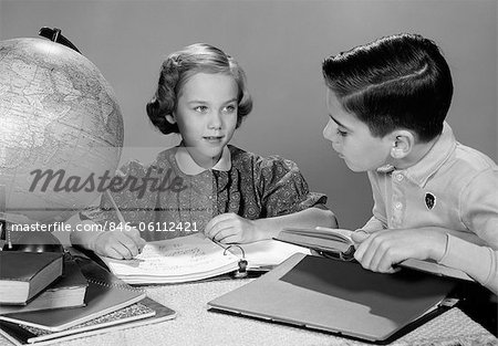 1960s BOY AND GIRL DOING HOMEWORK TOGETHER GLOBE AND BOOKS ON TABLE STUDIO INDOOR