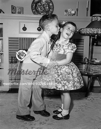 j1950s LITTLE BOY IN SUIT AND TIE TRYING TO KISS LITTLE GIRL IN PARTY DRESS