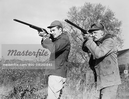 1940s 1950s MEN YOUNG SENIOR WITH SHOT GUNS AIMING TOWARDS CAMERA WEARING HUNTING CLOTHES & HATS