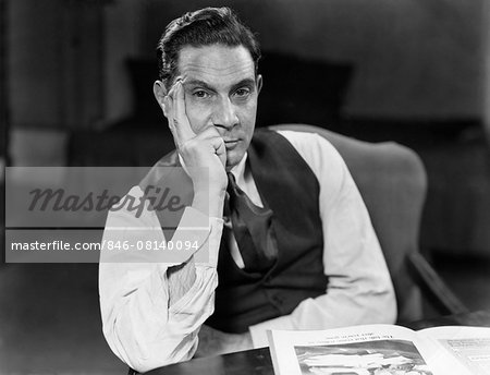 1930s 1940s MAN SEATED ELBOWS ON TABLE FACE LEANING ON HAND SERIOUS EXPRESSION WEARING SHIRT TIE VEST LOOKING AT CAMERA