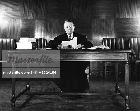 1940s MAN JUDGE READING PAPERS WEARING ROBE SEATED AT DESK