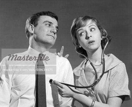 1960s WIFE WITH STETHOSCOPE ON HUSBAND 1960s WIFE WITH STETHOSCOPE ON HUSBAND