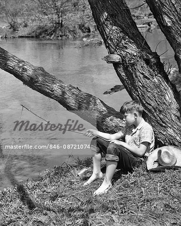 1940s BAREFOOT BOY SITTING UNDER TREE BY STREAM FISHING WITH TWIG POLE