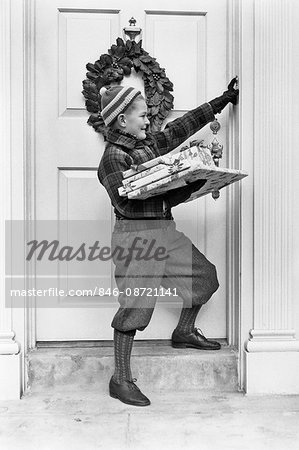 1930s 1940s BOY HOLDING WRAPPED PACKAGES RINGING BELL ON DOOR WITH CHRISTMAS WREATH