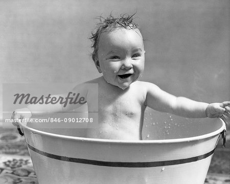 1920s 1930s SMILING HAPPY WET BABY GIRL SITTING BATHING IN METAL WASH TUB