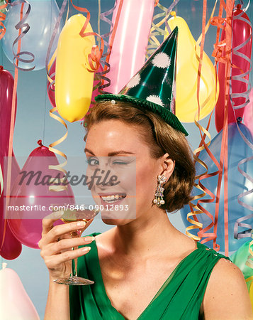 1960s BLOND WOMAN CELEBRATING NEW YEARS WEARING PARTY PAPER HAT DRINKING CHAMPAGNE LOOKING AT CAMERA WINKING EYE