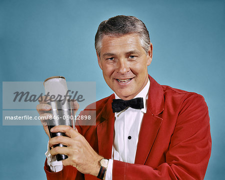 1960s 1970s SMILING MAN BARTENDER IN RED JACKET LOOKING AT CAMERA HOLDING COCKTAIL SHAKER MAKING MIXED DRINK 1960s 1970s SMILING MAN BARTENDER IN RED JACKET LOOKING AT CAMERA HOLDING COCKTAIL SHAKER MAKING MIXED DRINK