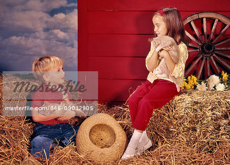 1960s LITTLE BOY AND GIRL BROTHER AND SISTER IN FARM SETTING HOLDING KITTENS