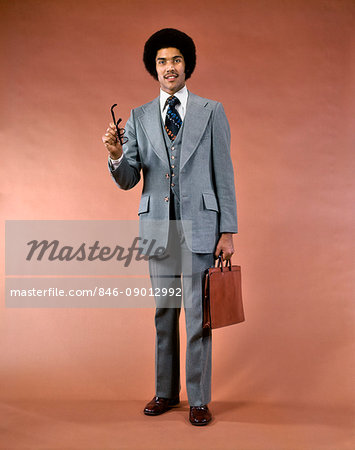 1970s SMILING AFRICAN AMERICAN MAN THREE PIECE SUIT BRIEFCASE LOOKING AT CAMERA POINTING GESTURING WITH EYEGLASSES