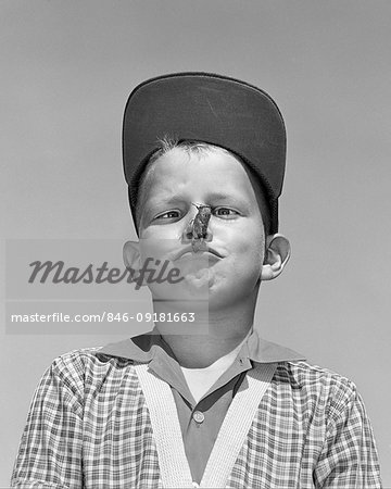 1950s CROSS EYED BOY WEARING BASEBALL CAP LOOKING AT BIG GRASSHOPPER PERCHED ON HIS NOSE