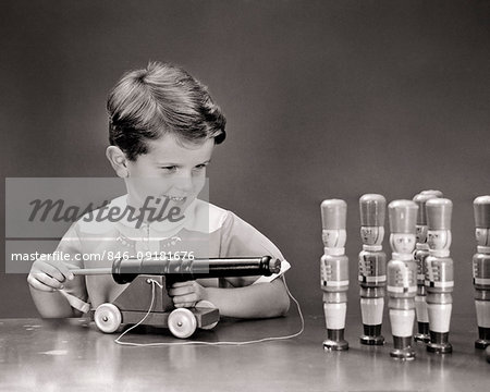 1940s SMILING BOY ABOUT TO SHOOT CORK POP GUN TOY CANNON INTO ROW OF TOY WOODEN SOLDIERS