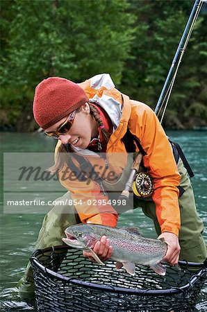 Woman holds a rainbow trout caught while fly fishing on the upper Kenai River on the Kenai Peninsula of Southcentral Alaska during Fall