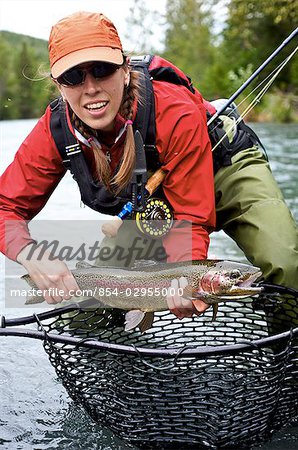 Woman holds a rainbow trout caught while fly fishing on the upper Kenai River on the Kenai Peninsula of Southcentral Alaska during Fall