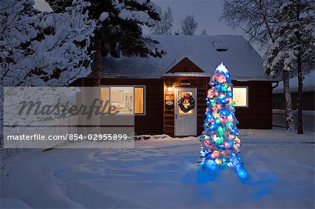 Family Home Covered In Snow With A Lit Christmas Tree In The Yard