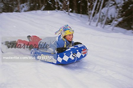 Young girl w/big smile on face sliding down hill on innertube Girdwood Southcentral Alaska Winter