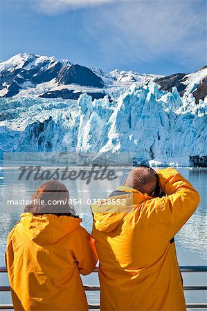 Tourist couple view scenery on a Klondike Express Glacier Cruise tour with Stairway glacier (r) flowing into Surprise Glacier in Harriman Fjord, Prince William Sound, Alaska