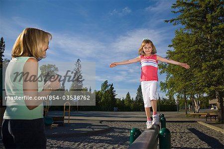 A mother watches as her young daughter walks on a  balance beam at a school playground in Anchorage, Alaska during Summer