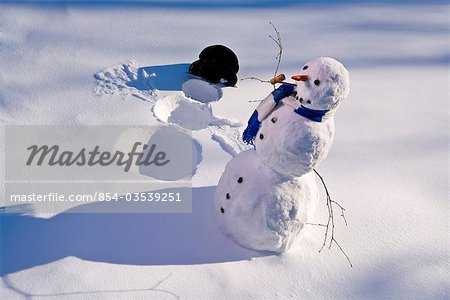 Snowman in forest making snow angel imprint in snow in late afternoon sunlight Alaska Winter