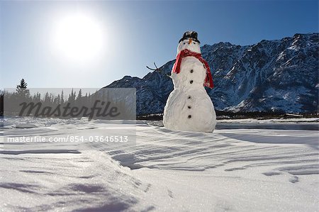 Snowman with a red scarf and black top hat sitting on the frozen Nenana River with the Alaska Range foothills in the background, Southcentral Alaska, Winter