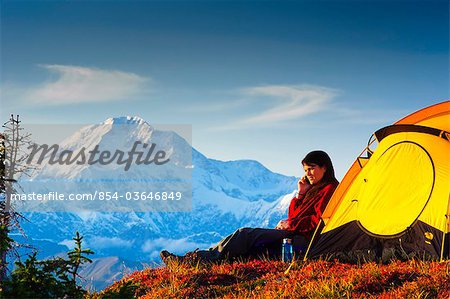 Woman talking on her cell phone while camping with the south summit of Mt. McKinley in the background, Peters Hills, Denali State Park, Southcentral Alaska, Fall/n