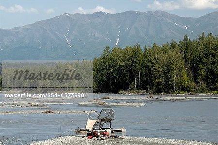 Two men relax on a gravel bar next to an aluminum fish wheel on the Matanuska River, Mat-Su Valley, Southcentral Alaska, Summer