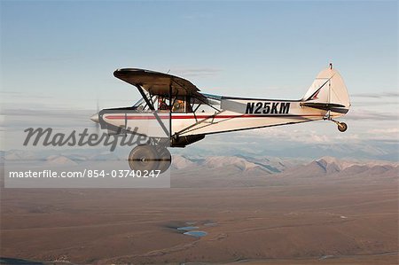 Aerial view of a Piper Super Cub airplane flying over the Jago River and tundra of the coastal plain in ANWR with the Romanzof Mountains in the background, Arctic Alaska, Summer
