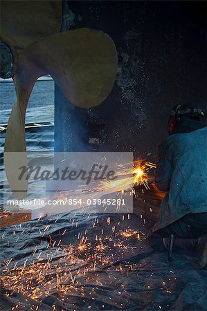 Worker cuts metal fittings off a boat hull using an oxy-acetylene cutting torch, Kodiak Boatyard, Saint Herman Harbor, Kodiak, Near Island, Southwest Alaska, Autumn