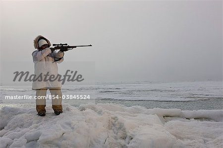 Female Inupiaq Eskimo hunter wearing a Eskimo parka(Atigi) aims a rifle towards the open water of the Chukchi Sea, Barrow, Arctic Alaska, Summer