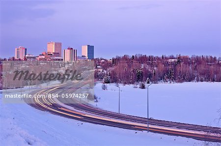 The downtown Anchorage skyline overlooking Westchester Lagoon with traffic on Minnesota Blvd. at twilight, Southcentral Alaska, Winter