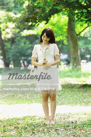 Young Woman Standing in Forest Holding Flowers