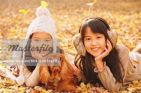 Preteen Girls Lying Down In Leaves With Dog