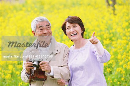 Middle-Aged Japanese Couple Snapping In Field Of Wildflowers