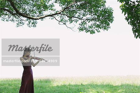 Asian woman playing the violin in a grass field