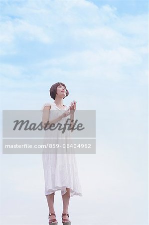 Japanese woman with short hair in a white dress standing and holding a Smartphone