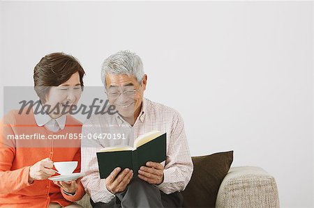 Senior adult couple having a coffee while reading a book on the sofa
