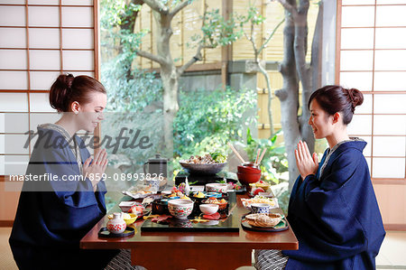 Caucasian woman wearing yukata eating with Japanese friend at traditional ryokan, Tokyo, Japan