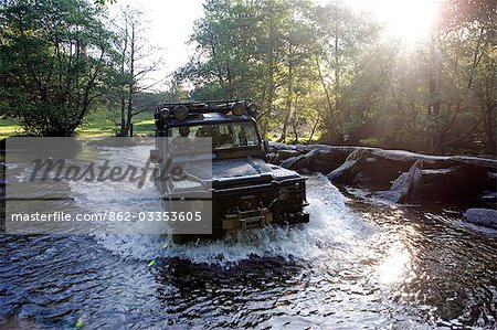 England,Somerset,Exmoor. The ford at Tarr Steps is waded by a four wheel drive - a Landrover Defender 110 with the prehistoric clapper bridge on the right hand side.