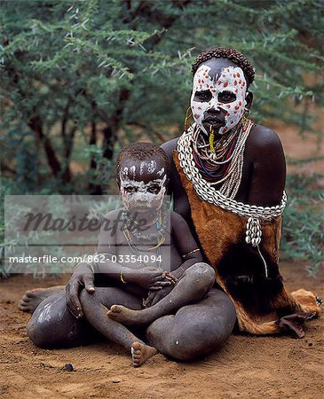 A Karo woman sits with child. A small Omotic tribe related to the Hamar,who live along the banks of the Omo River in southwestern Ethiopia,the Karo are renowned for their elaborate body painting using white chalk,crushed rock and other natural pigments. Typically for a Karo woman,the mother has ochred her hair in tight ringlets and has a ring through her bottom lip.
