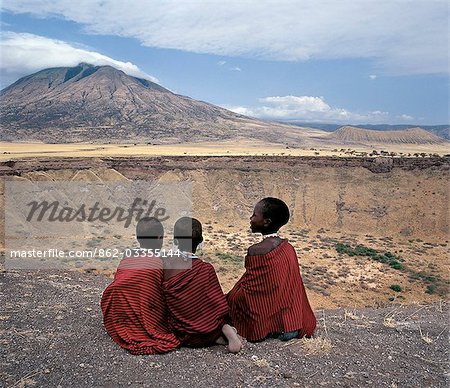 Three Maasai girls sit on the edge of Shimu la Mungu (a volcanic blow hole known as 'God's hole') with the extinct volcano,Kerimasi,in the distance.