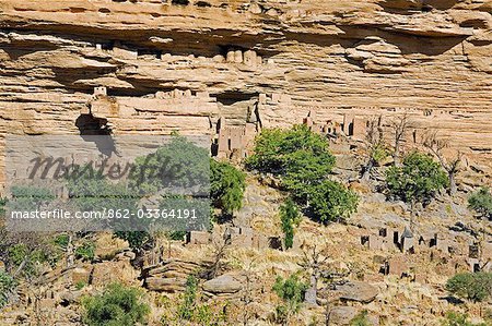 Mali,Dogon Country,Banani. Part of the Dogon village of Banani situated at the foot of the 120-mile-long Bandiagara escarpment. The Dogon’s burial caves are sited in the almost inaccessible sheer sandstone cliffs behind the village. The caves were originally used by the Tellem who were driven out by the Dogon in the fifteenth century.