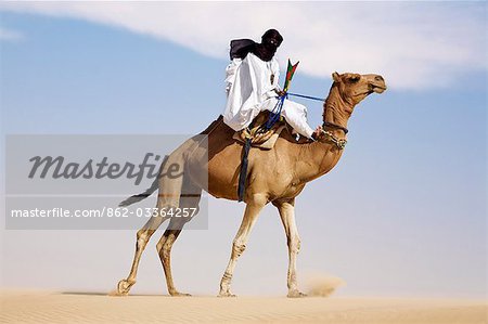 Mali,Timbuktu. In the desert north of Timbuktu,a Tuareg man rides his camel across a sand dune He steers the animal with his feet.