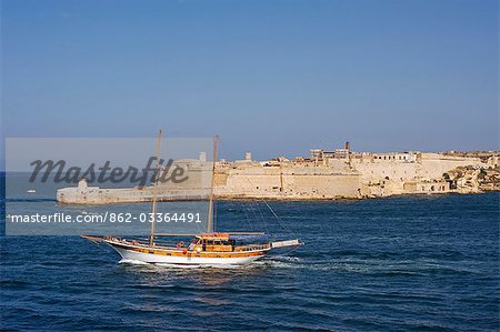 Malta,Valletta. A fishing boat motors out of the entrance to the Grand Harbour past Ricasoli Point.
