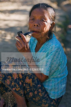 Myanmar,Burma,Mrauk U. An old That woman smoking a pipe at Mrauk U. That women traditionally pierce and extend their earlobes to insert metal hoops.